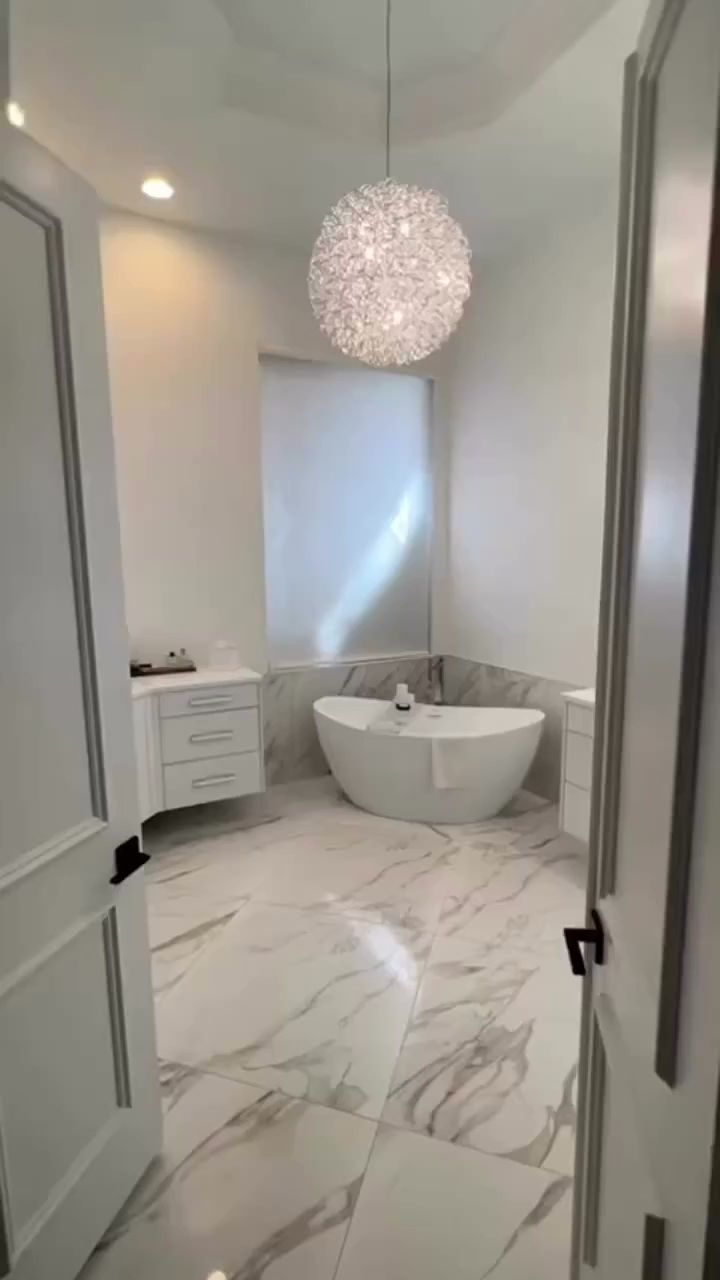 R&B project: freestanding tub under a crystal chandelier on marble-look floor tile, seen through double doors