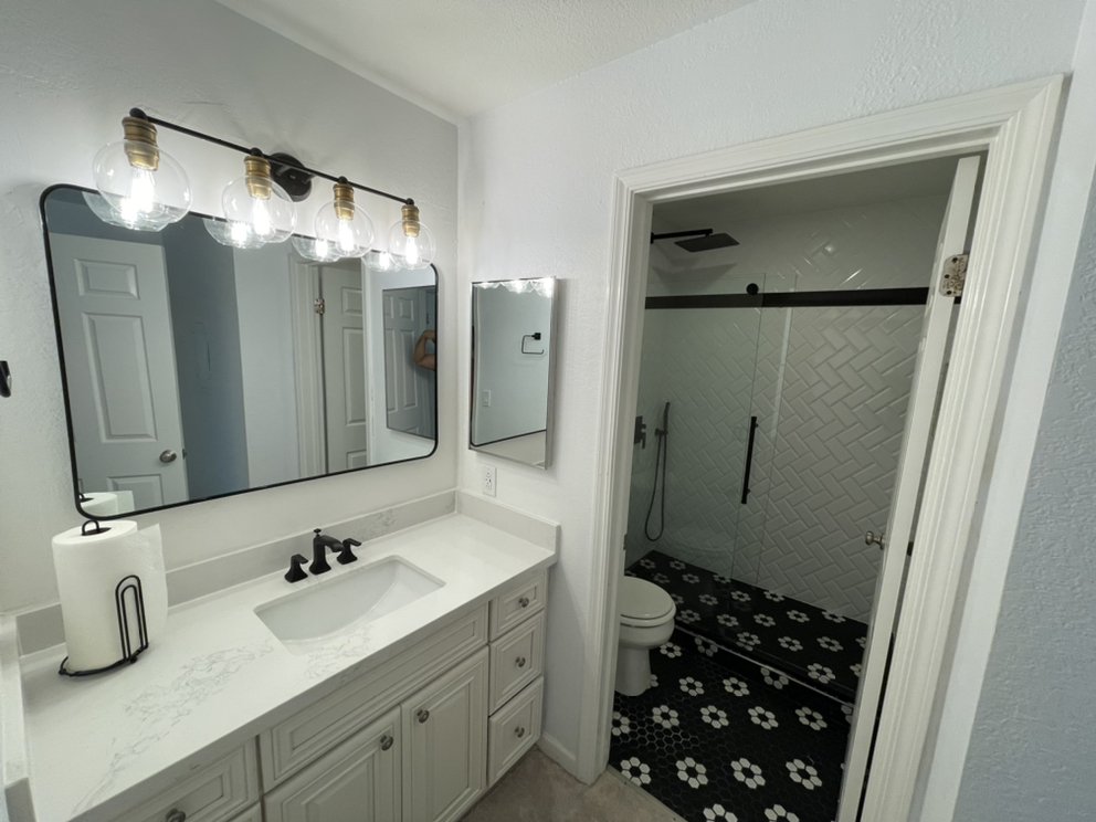 R&B project: white vanity with a black faucet beside a toilet room with black and white patterned floor tile