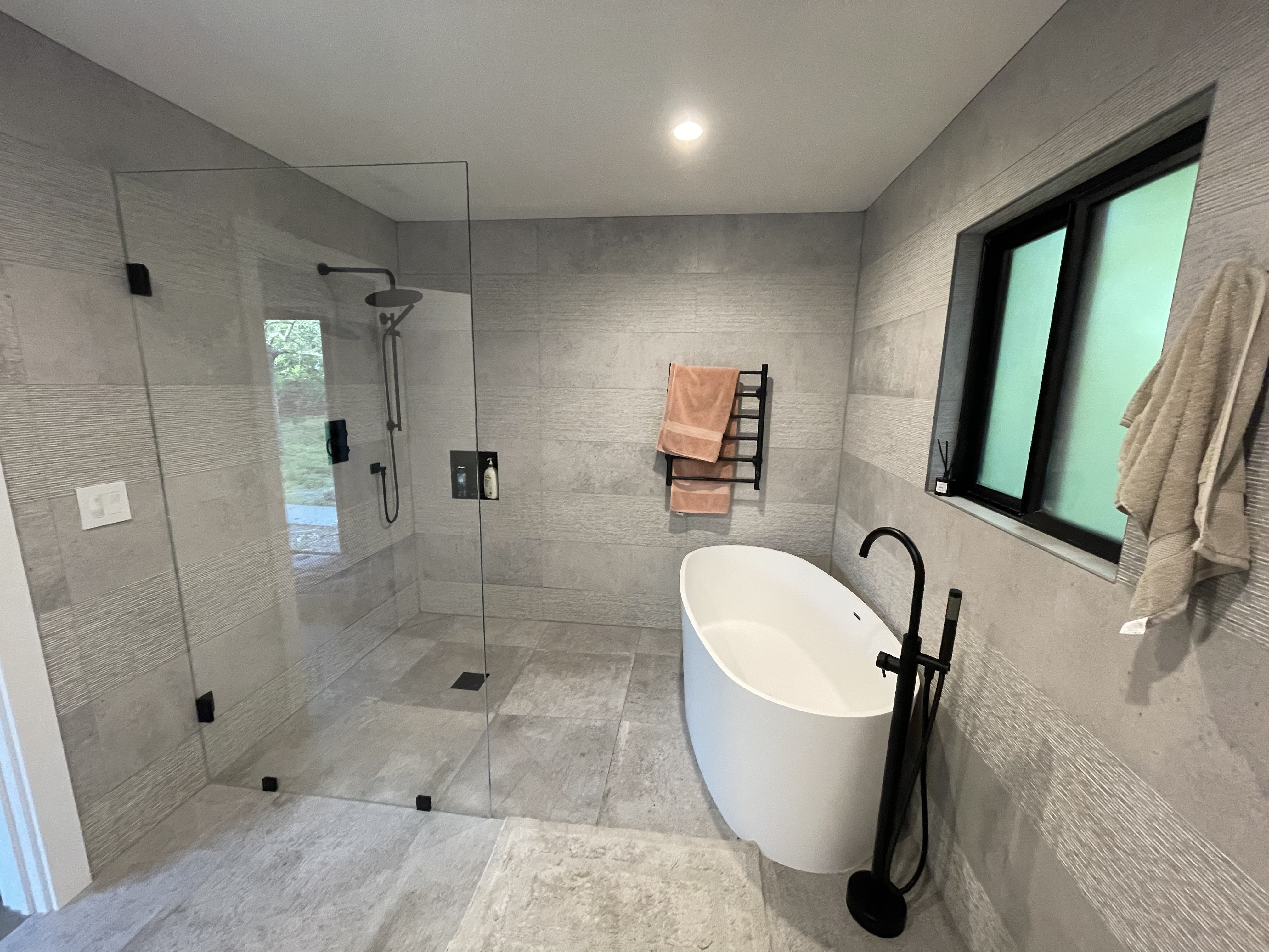 R&B project: glass shower and freestanding tub with a black floor-mounted faucet below a black window