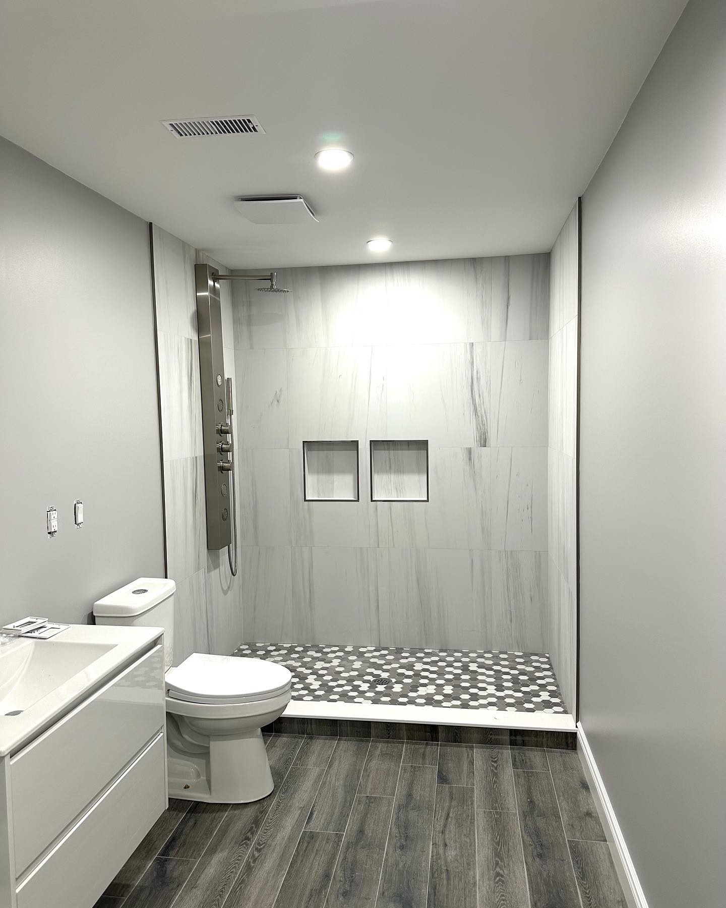 R&B project: long bathroom with a glass shower, two niches and a pebble floor next to gray wood-look flooring