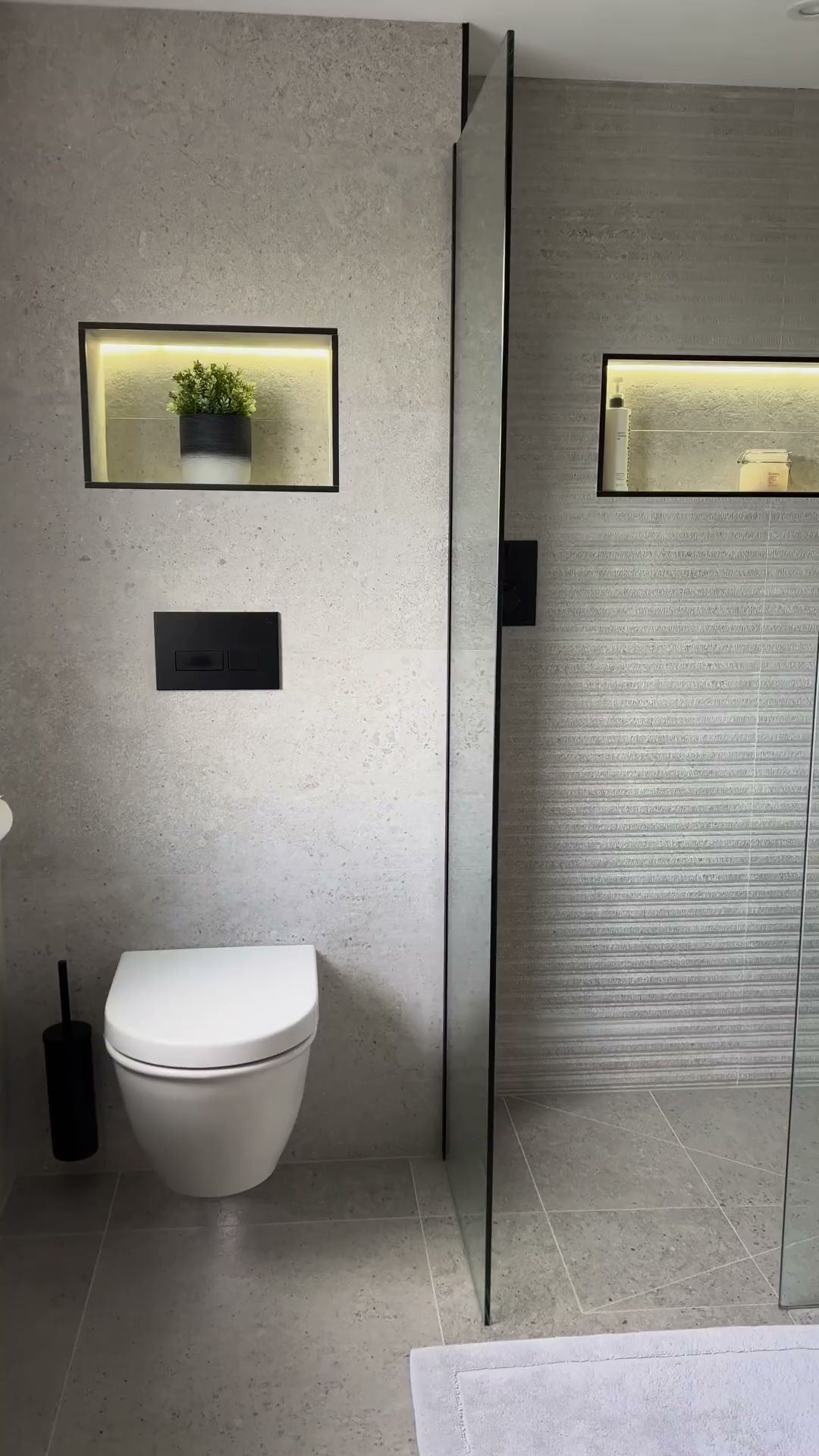 R&B project: wall-hung toilet beside lit wall niches in gray tile