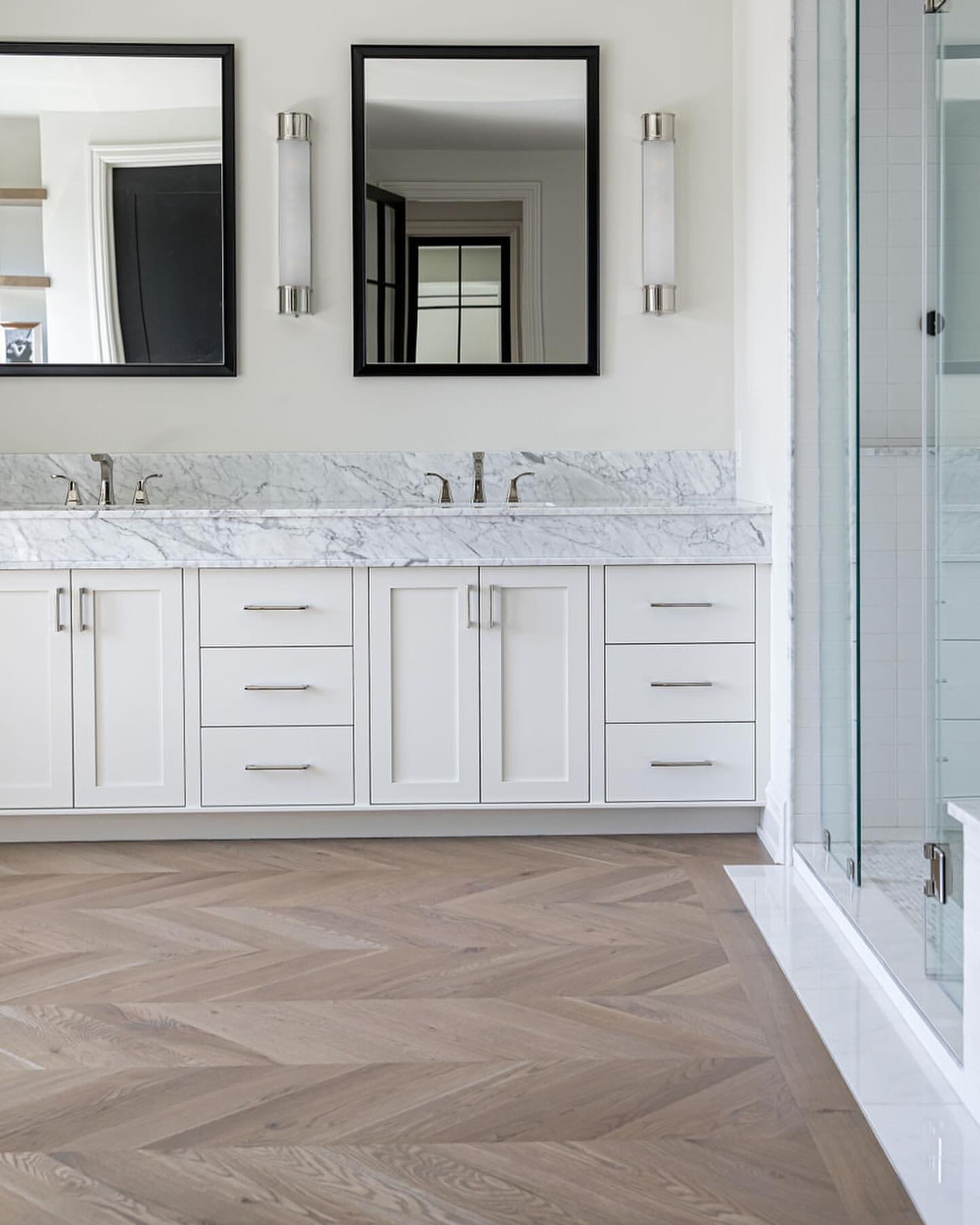 R&B project: white double vanity with a marble top on a herringbone wood floor, glass shower at the edge
