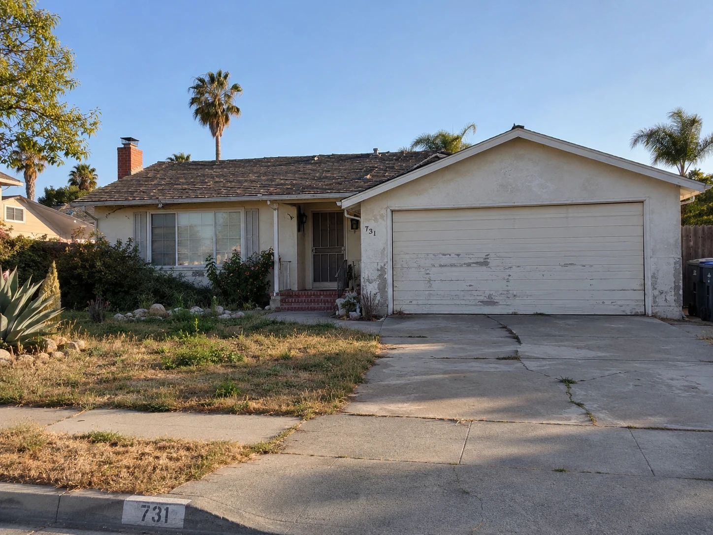 Before concept: a California ranch home with worn stucco, an aging roof, a peeling garage door and a cracked driveway